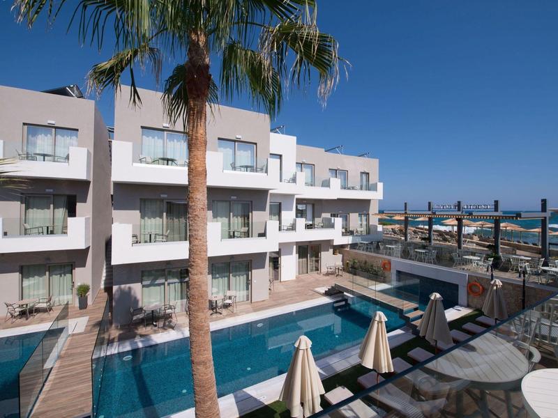 Hotel con piscina, lettini e palme sotto il sole vicino al mare.