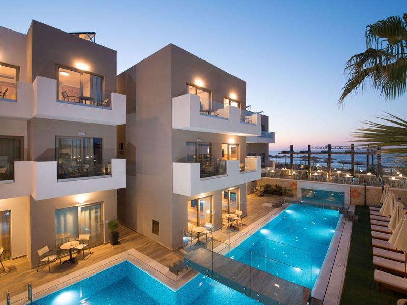 Complesso alberghiero moderno con piscine illuminate al tramonto e vista sul mare.