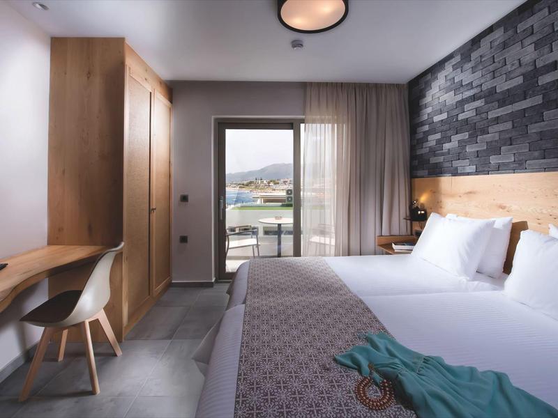 Camera d'hotel moderna con letto matrimoniale, scrivania e balcone con vista sulle montagne.