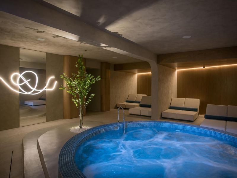 Modern wellness area with jacuzzi, sofas, and subdued lighting.