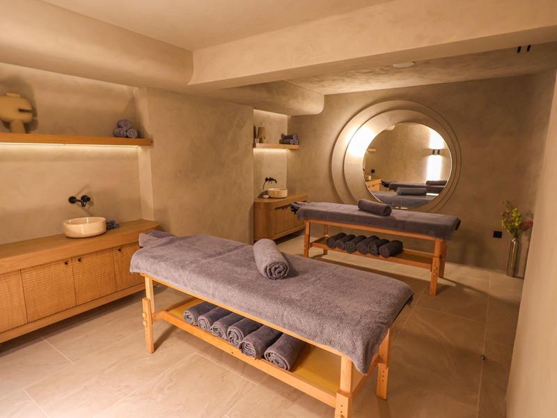 Modern wellness room with massage table, towels, and a round mirror.
