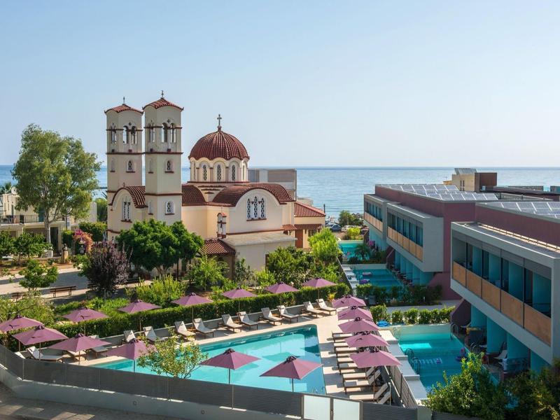 Hotel complex with pool, sun loungers, and church by the sea under clear sky