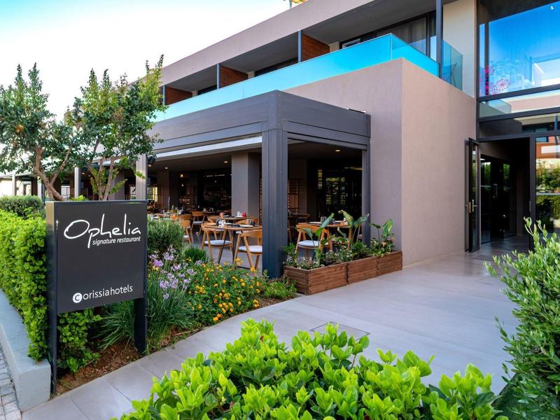 Modern hotel building with terrace and seating area surrounded by well-maintained greenery.