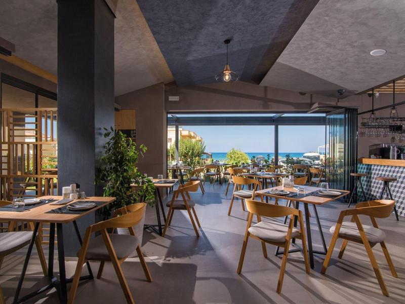 Modern restaurant with wooden furniture and large windows overlooking the sea.