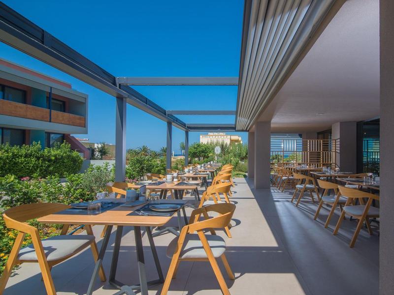 Modern outdoor area of a hotel restaurant with tables and wooden chairs under a blue sky.
