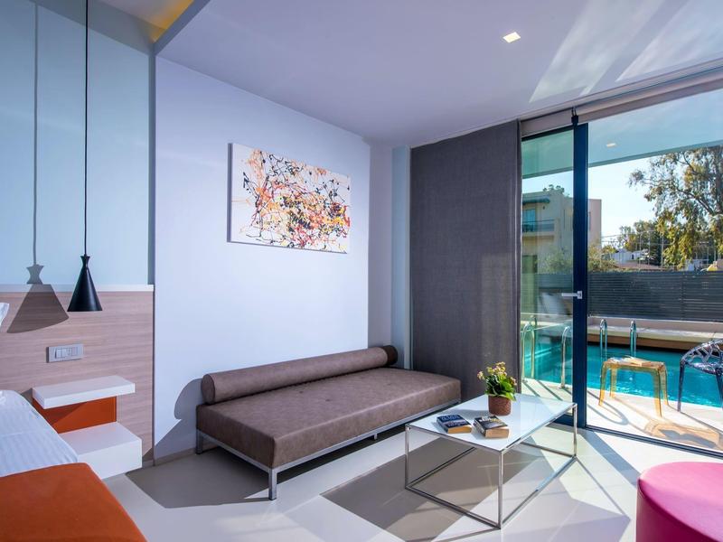 Modern hotel room with sofa, table, balcony, and pool view in daylight.