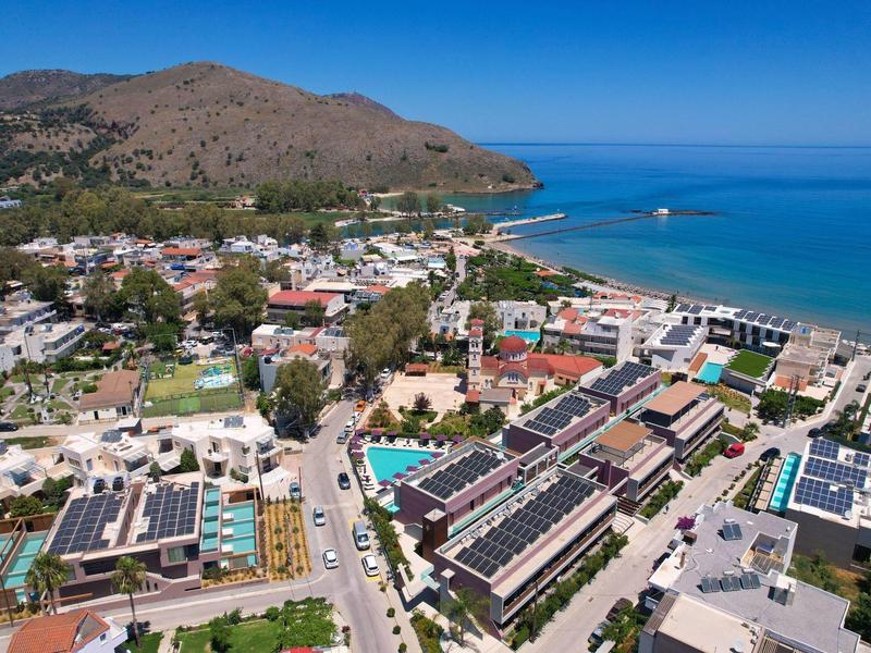 Aerial view of a coastal town with a beach and mountains in the background on a sunny day.