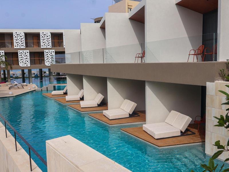 Modern hotel pool with private sunbathing areas directly by the water under blue sky.