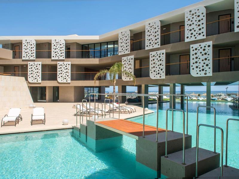 Modern hotel with pool and balcony featuring decorative white panels in sunny weather.