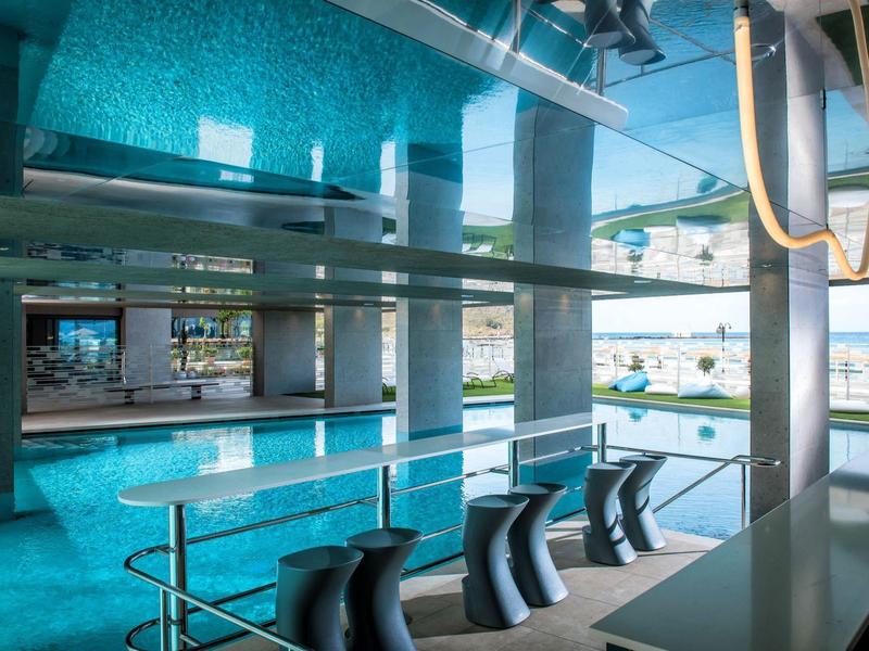 Interior view of a modern swimming pool with bar stools and window view of outdoor area.