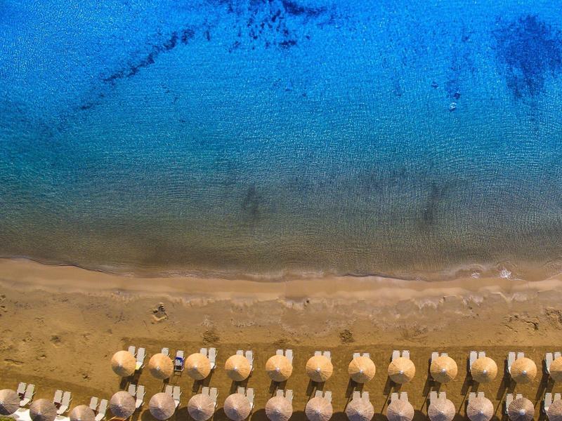 Aerial view of a beach section with rows of sun loungers and blue water.