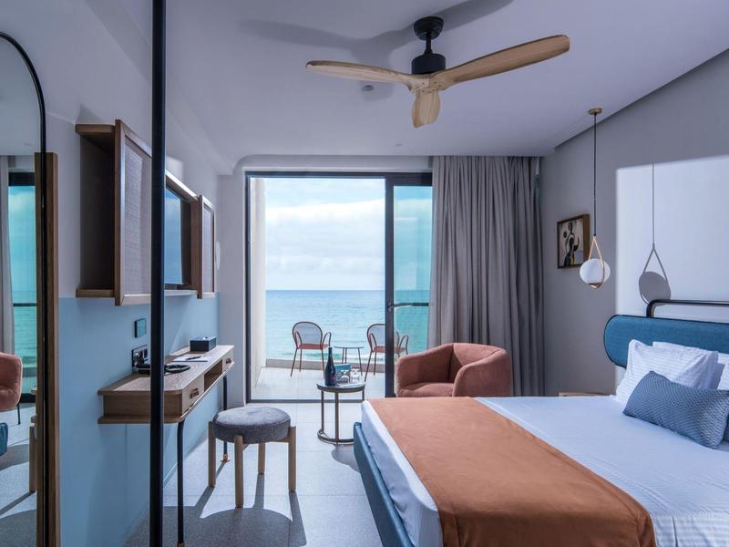Modern hotel room with large bed, balcony, and sea view.