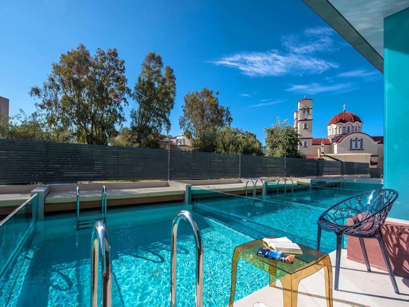 Clear swimming pool with chairs on the terrace and church in the background under blue sky.