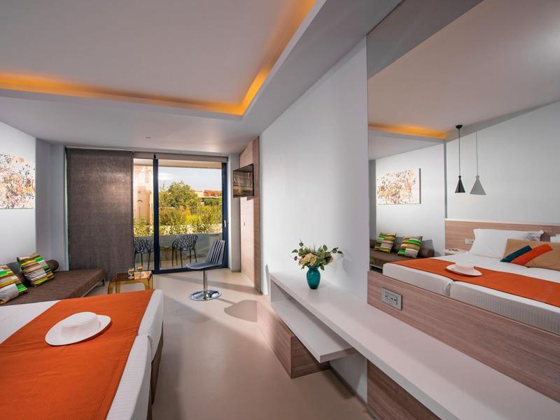 Modern hotel room with large bed, sofa, and balcony overlooking green trees.