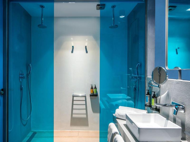 Modern hotel bathroom with blue glass showers and white sinks.