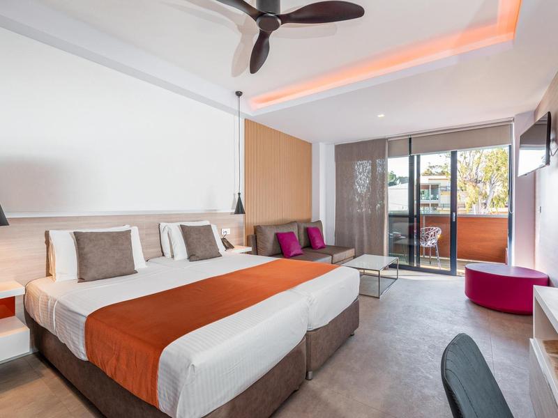 Modern hotel room with two single beds, balcony, and cozy seating area.