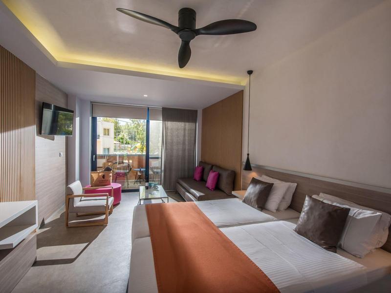 Modern hotel room with double bed, ceiling fan, seating area, and balcony.