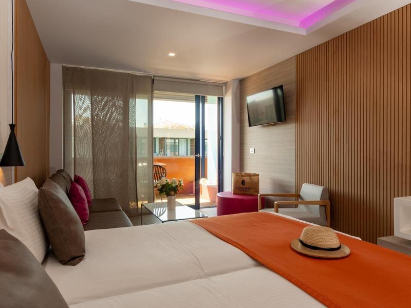 Modern hotel room with large beds, wooden accents, and balcony access with sea view.