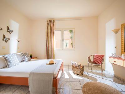 Světle hotelový pokoj s velkou postelí, proutěným křeslem, zrcadlem a dekoracemi na stěně s motýly.