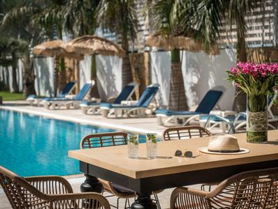 Terrazza della piscina con sedie, ombrelloni e tavolo apparecchiato con cappello e fiori
