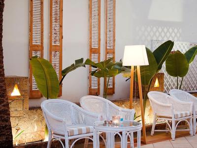 Accoglienti mobili in vimini bianchi con lampada su terrazza davanti a muro bianco con persiane in legno