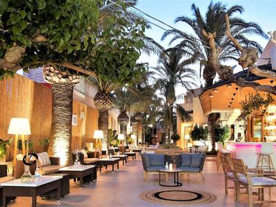 Area hotel aperta con posti a sedere, bar e palme alla luce della sera.