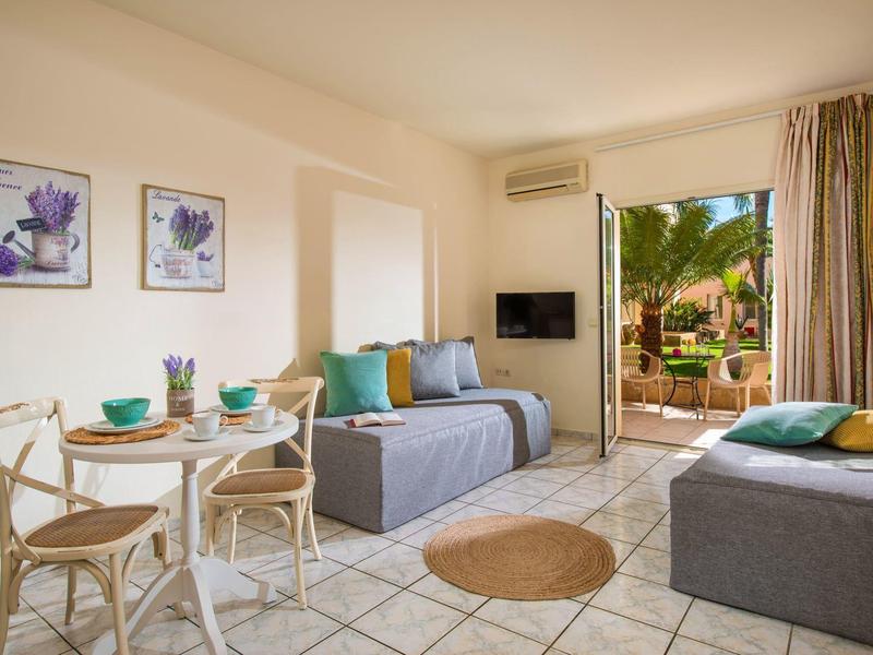 Světý obývací pokoj s posezením, jídelním stolem a přístupem na hotelovou terasu.