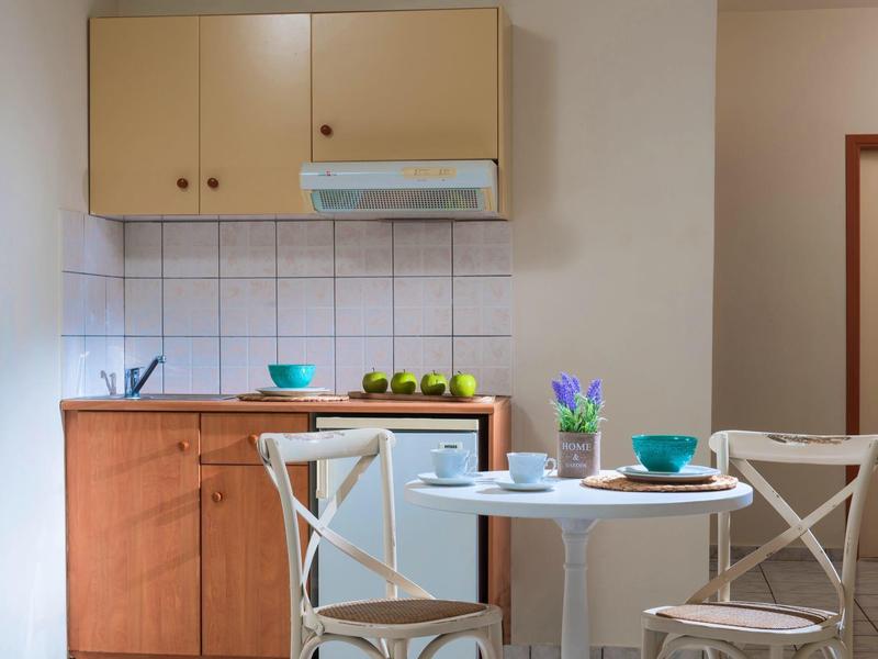 Malá kuchyň s dřevěnými skříňkami vedle bílého stolu se dvěma židlemi a prostřenými talíři