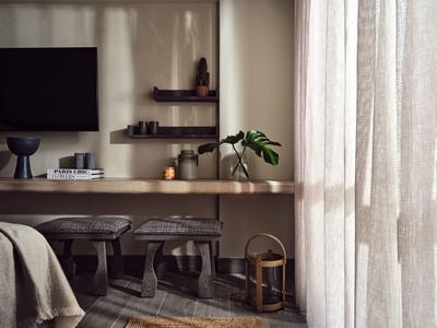 Gemütliches Wohnzimmer mit Fernseher, Holztisch, Hockern, Vorhängen und minimaler Dekoration.