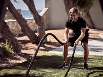 Uomo che si allena con corde da battaglia all'aperto su prato vicino ad alberi e muro di pietra