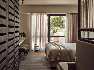 Schlicht eingerichtetes Schlafzimmer mit großem Fenster, Vorhängen und Bett mit beiger Decke.