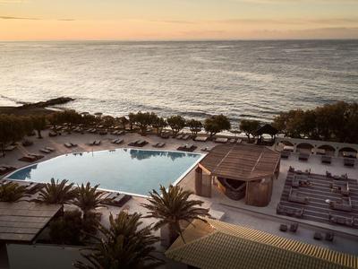 Poolbereich mit Liegestühlen und Palmen nahe dem Meer bei Sonnenuntergang.