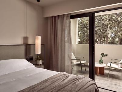 Camera d'hotel con letto grande e accesso a balcone con sedie e tavolo.