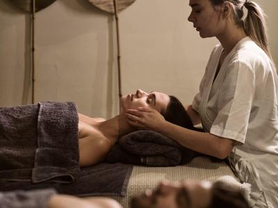 Zwei entspannt liegende Personen erhalten im Spa Gesichts- und Kopfmassagen in ruhigem Ambiente.