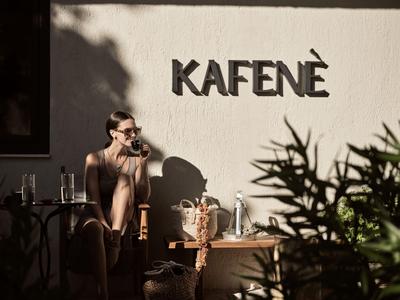Person relaxes in natural light in front of a wall with the sign KAFENÈ.