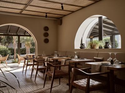 Cozy hotel restaurant with wooden furniture and large round windows letting in daylight.