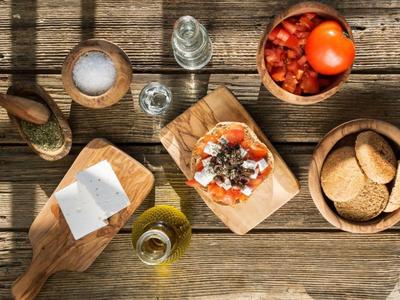Ansicht von einem rustikalen Holztisch mit Brot, Tomaten, Olivenöl und Salz in Holzschalen.