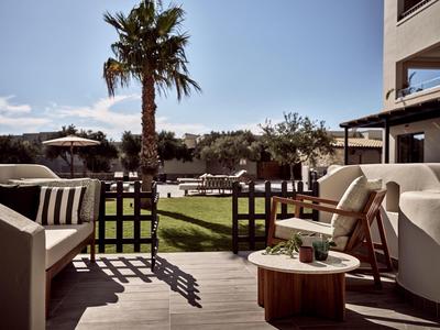 Terrasse mit Sitzmöbeln, Holztisch, Palmen und gepflegtem Rasen bei sonnigem Wetter.