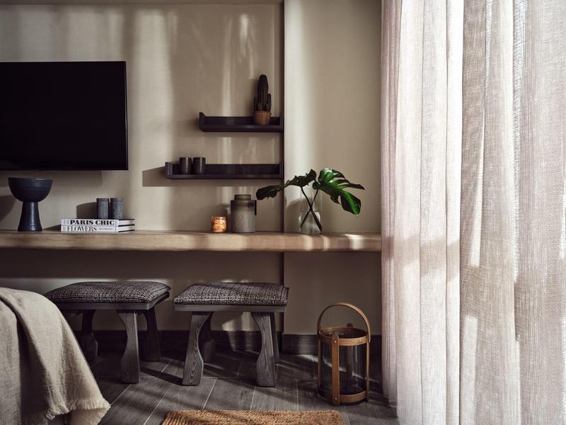 Gemütliches Wohnzimmer mit Fernseher, Holztisch, Hockern, Vorhängen und minimaler Dekoration.