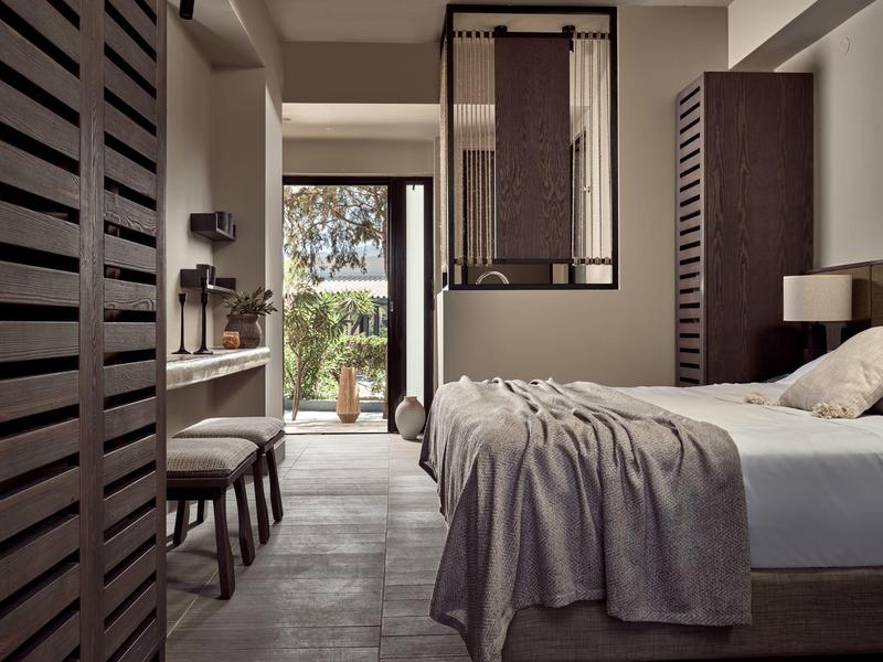 Modernes Schlafzimmer mit Holzakzenten, grauer Bettdecke und Zugang zu einem Garten im Hintergrund.