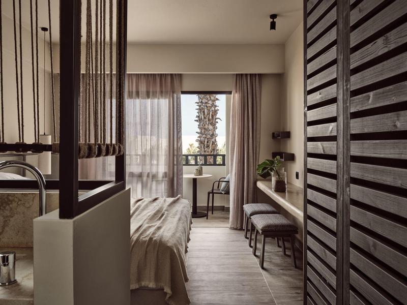 Modernes Schlafzimmer mit großem Fenster, Tisch, Stuhl, gemütlichem Bett und Holzlamellen-Tür.