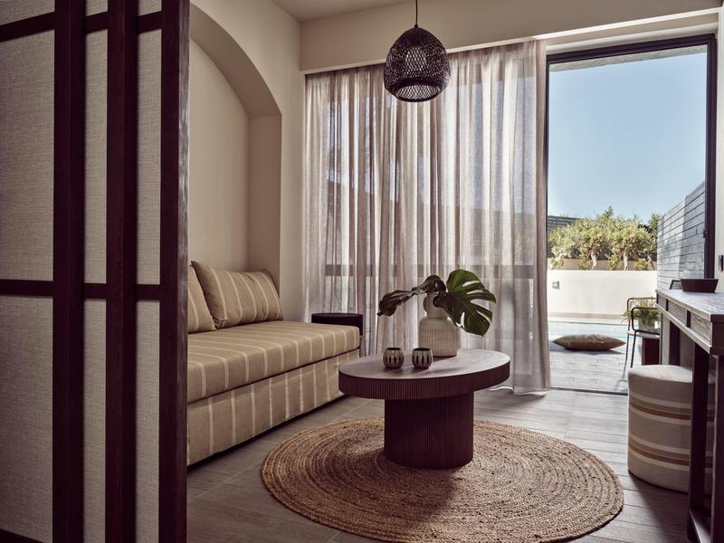 Gemütliches Wohnzimmer mit gestreiftem Sofa, rundem Holztisch und großem Fenster mit Blick auf Balkon.