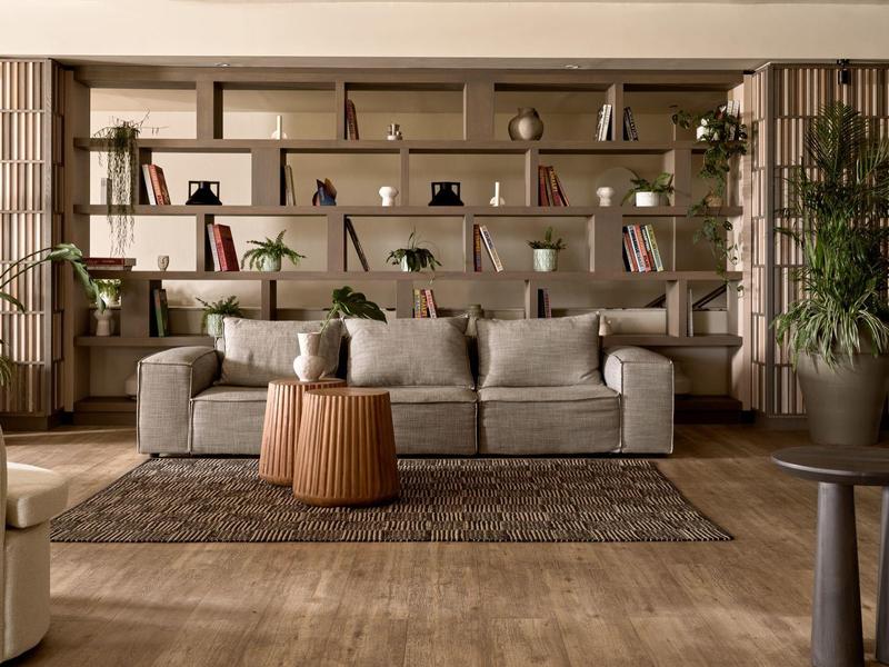Modernes Wohnzimmer mit grauem Sofa, Holzregal, Teppich und grünen Pflanzen, helle Holzböden.