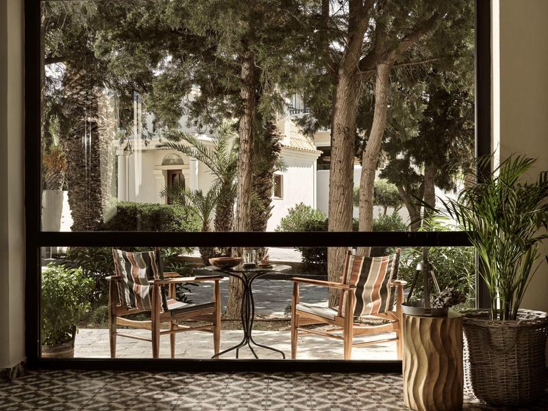 Terrasse mit zwei Holzstühlen, Metalltisch, großen Bäumen und Häusern im Hintergrund.