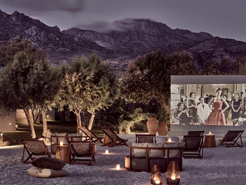 Outdoor-Kino mit Stühlen, Kerzen und Bäumen vor Bergen bei Dämmerung.