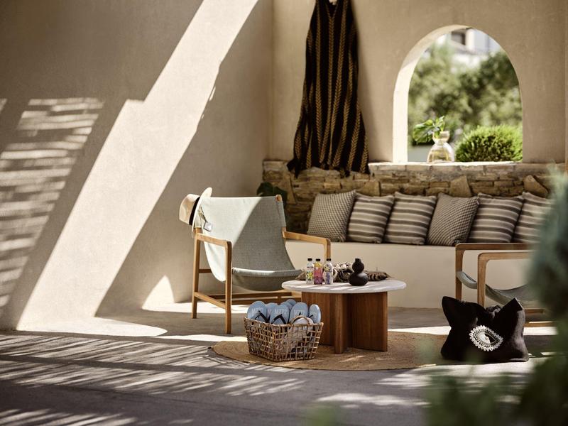 Gemütliche Sitzecke mit Holzstuhl, Kissen, Korb und runden Holztisch in hellem Raum.