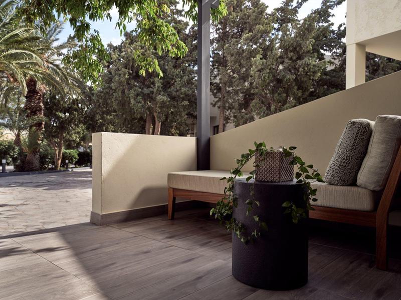 Moderner Außenbereich mit Holzboden, Sitzbank, grauen Kissen und Pflanzen im Pflanzgefäß.