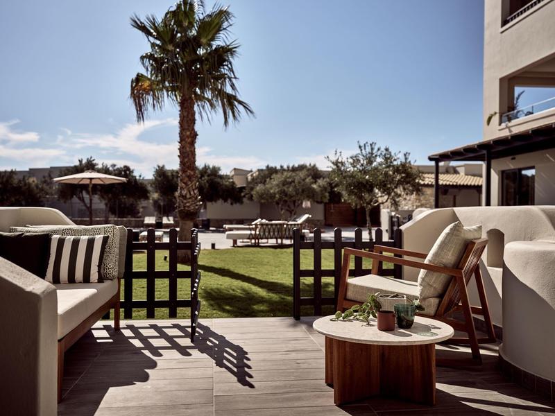 Terrasse mit Sitzmöbeln, Holztisch, Palmen und gepflegtem Rasen bei sonnigem Wetter.