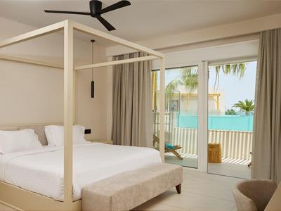 Bright hotel room with four-poster bed and terrace overlooking the sea.