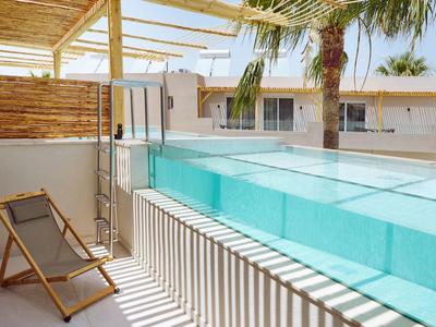 Modern pool area with glass swimming pool, wooden chairs, and palm trees on the terrace.